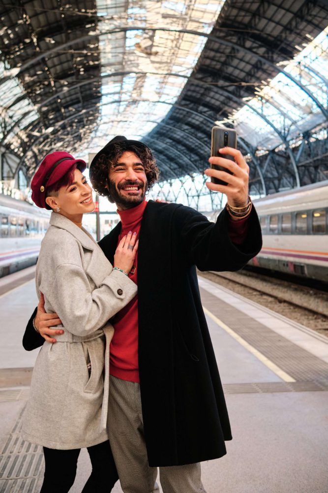 Vertical portrait of a happy couple taking a selfie into a train station